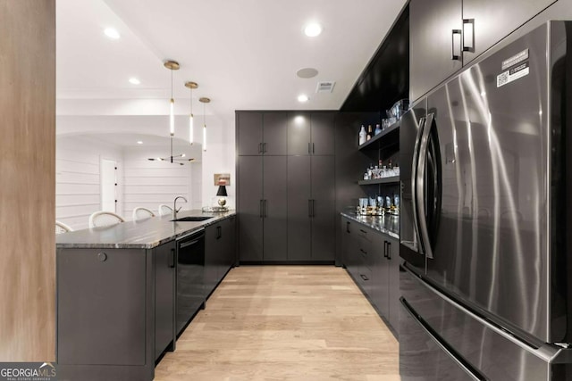 kitchen with dishwasher, dark stone countertops, a peninsula, freestanding refrigerator, and a sink