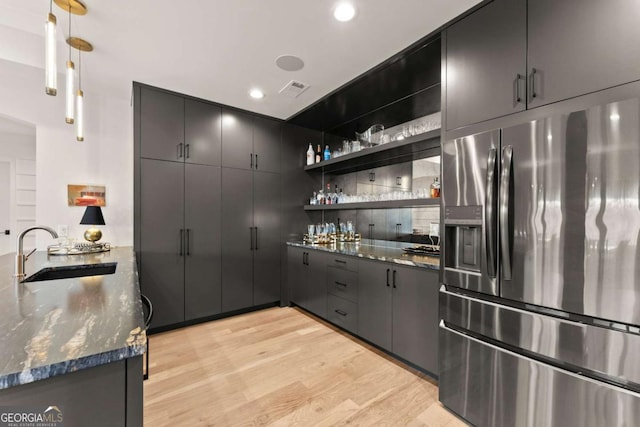 kitchen with a sink, dark stone counters, a peninsula, stainless steel fridge with ice dispenser, and light wood finished floors
