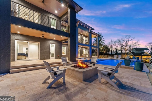 patio terrace at dusk with a balcony, a fire pit, and a fenced in pool
