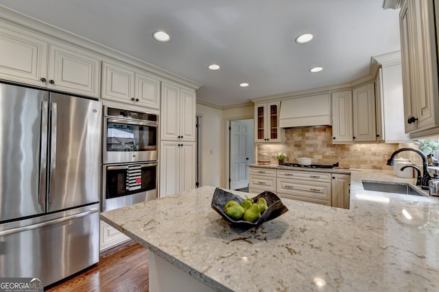 kitchen with cream cabinetry, a sink, light stone counters, appliances with stainless steel finishes, and custom exhaust hood