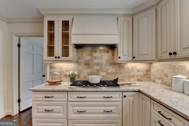 kitchen with decorative backsplash, custom exhaust hood, light stone counters, and stainless steel gas cooktop