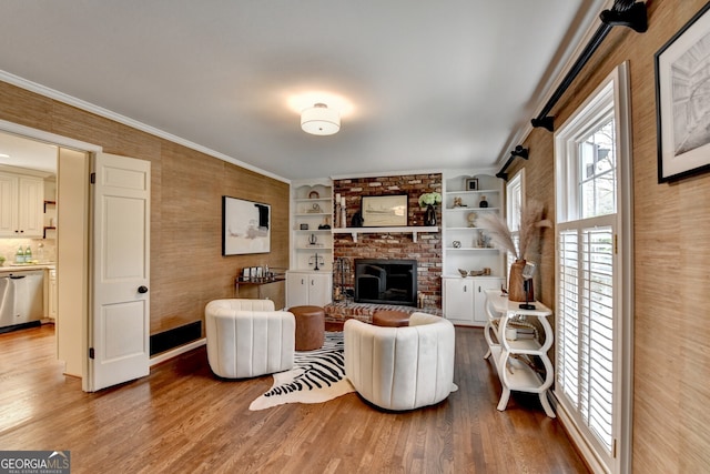 living area featuring crown molding, a brick fireplace, and light wood-type flooring