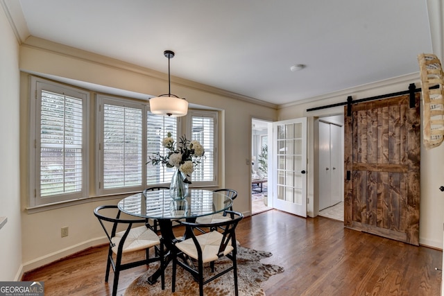 dining area with crown molding, a barn door, wood finished floors, and baseboards