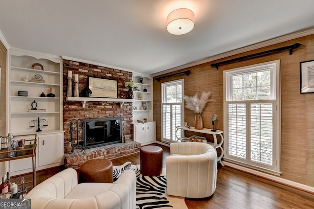 living area with built in features, a brick fireplace, crown molding, and wood finished floors