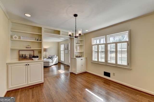 unfurnished dining area with baseboards, a chandelier, built in features, ornamental molding, and wood finished floors