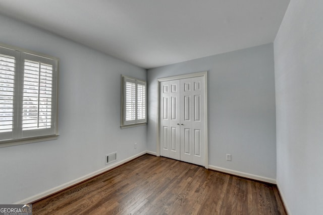 unfurnished bedroom with visible vents, baseboards, a closet, and dark wood-style floors