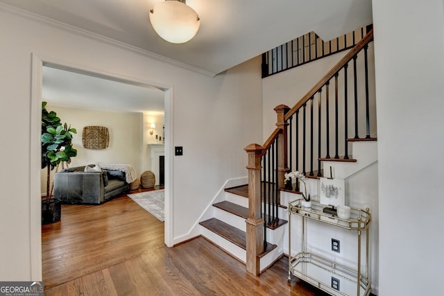 stairs with a fireplace, wood finished floors, baseboards, and ornamental molding