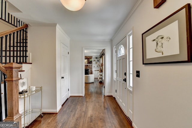 foyer entrance featuring a brick fireplace, stairway, wood finished floors, and ornamental molding