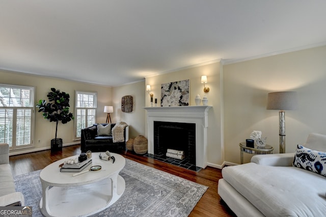 living area with a tiled fireplace, ornamental molding, baseboards, and wood finished floors