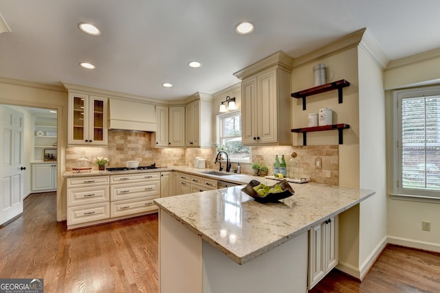 kitchen featuring custom range hood, a peninsula, cream cabinetry, gas cooktop, and a sink