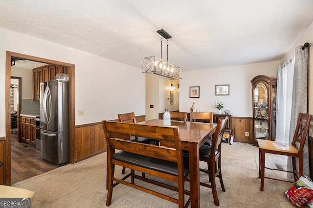 dining space with a wainscoted wall, light colored carpet, a textured ceiling, and wood walls