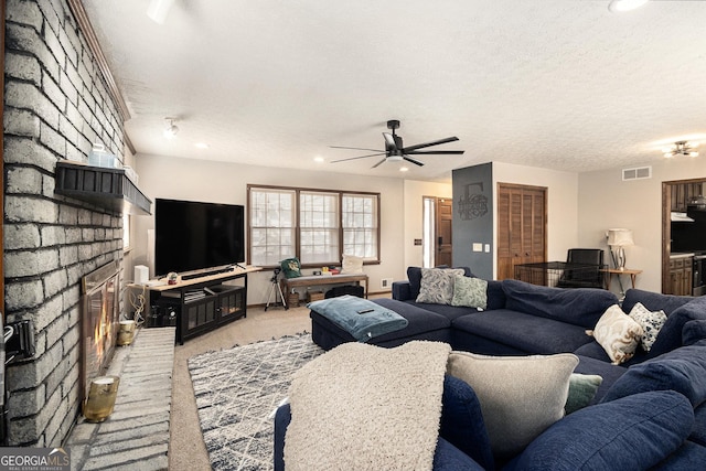 living room with visible vents, ceiling fan, a textured ceiling, a brick fireplace, and light colored carpet