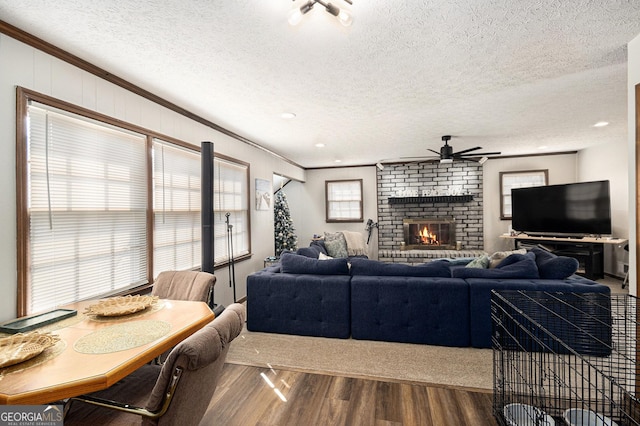 living room featuring a brick fireplace, ornamental molding, wood finished floors, a textured ceiling, and a ceiling fan