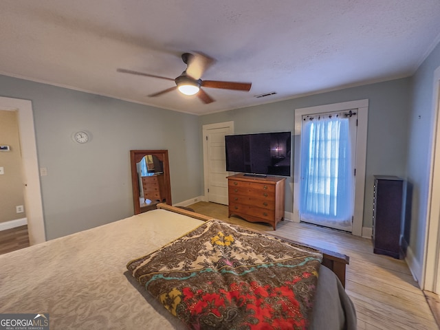 bedroom with light wood finished floors, visible vents, baseboards, ornamental molding, and a ceiling fan