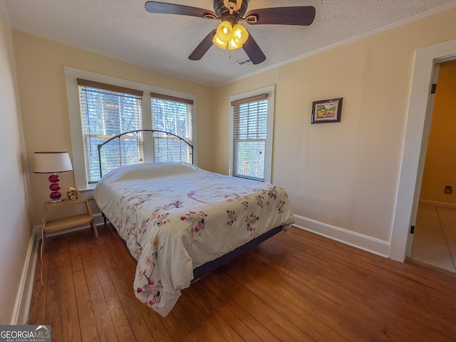 bedroom with a baseboard heating unit, wood-type flooring, a textured ceiling, and baseboards