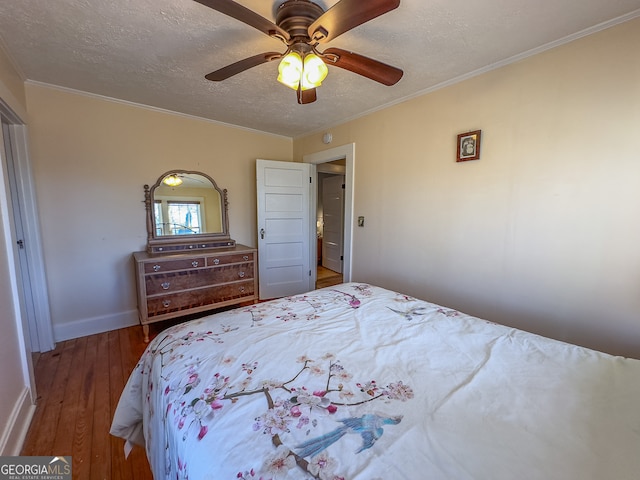 bedroom with a ceiling fan, a textured ceiling, wood-type flooring, crown molding, and baseboards