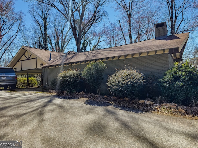 view of side of home featuring brick siding, roof with shingles, and a chimney