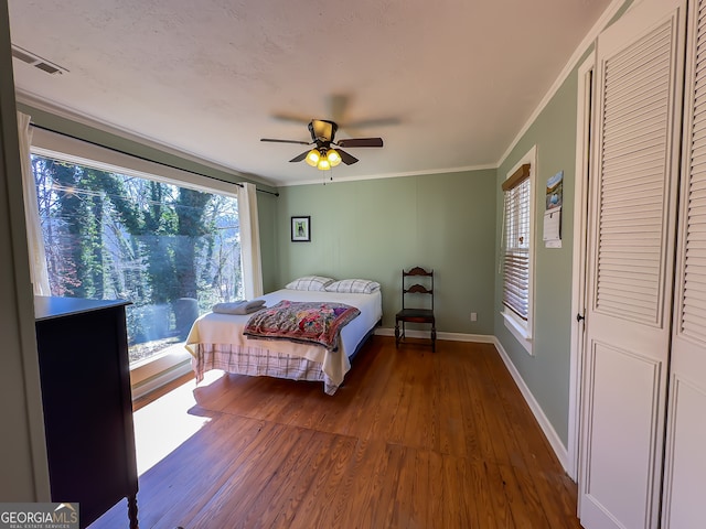 bedroom featuring visible vents, a ceiling fan, wood finished floors, crown molding, and baseboards