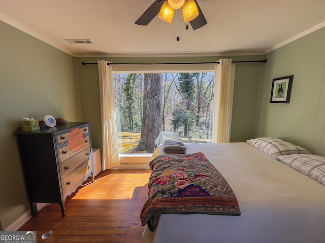 bedroom featuring visible vents, ornamental molding, a ceiling fan, hardwood / wood-style flooring, and baseboards