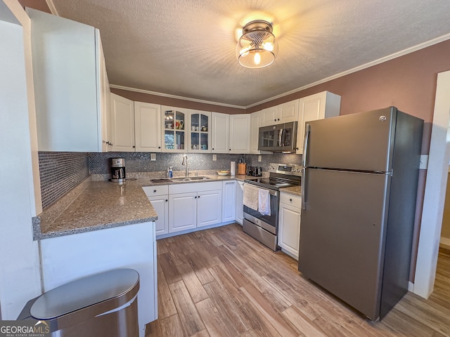 kitchen featuring a sink, tasteful backsplash, white cabinetry, stainless steel appliances, and light wood finished floors