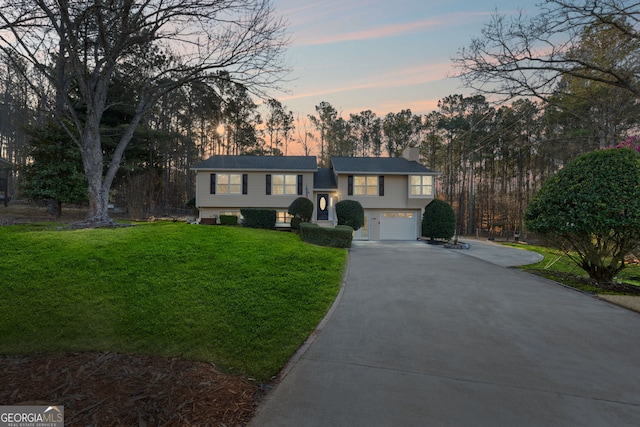 bi-level home with driveway, a lawn, a chimney, and an attached garage