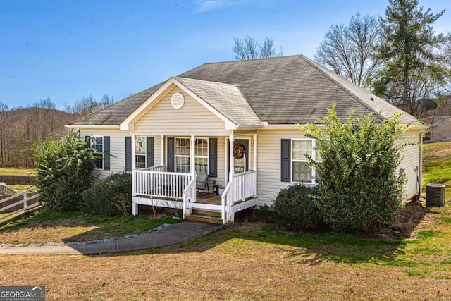 view of front of home with central air condition unit, covered porch, a front lawn, and fence