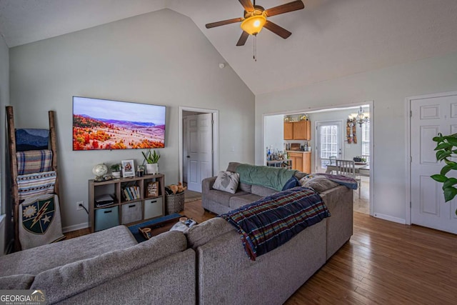 living area with ceiling fan with notable chandelier, high vaulted ceiling, baseboards, and wood finished floors