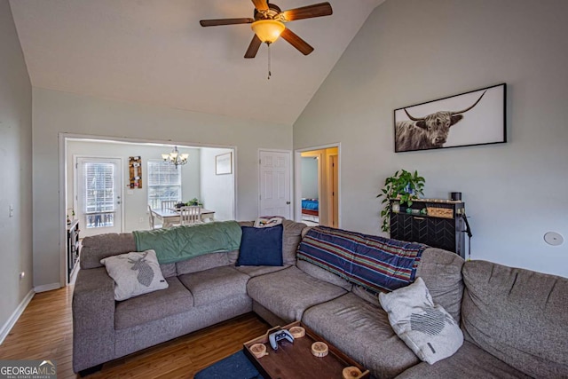 living room with ceiling fan with notable chandelier, wood finished floors, baseboards, and high vaulted ceiling