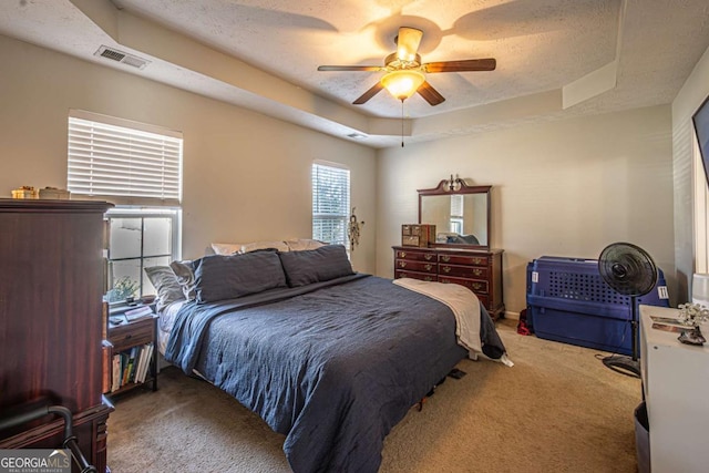 carpeted bedroom featuring visible vents, ceiling fan, a textured ceiling, and a tray ceiling