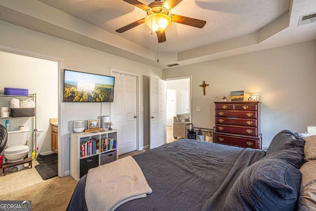 bedroom featuring ensuite bath, a tray ceiling, visible vents, and a textured ceiling