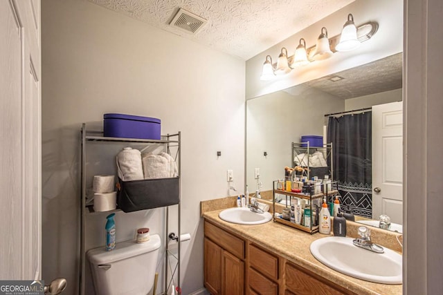 bathroom featuring a textured ceiling, toilet, visible vents, and a sink