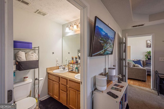 ensuite bathroom with visible vents, toilet, a sink, a textured ceiling, and double vanity