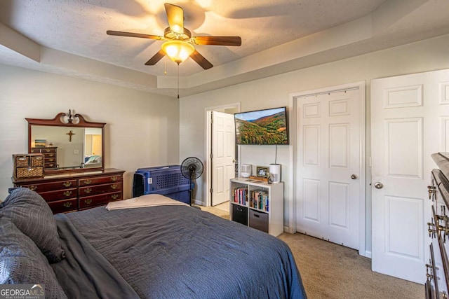 bedroom with a tray ceiling, light carpet, a textured ceiling, and ceiling fan