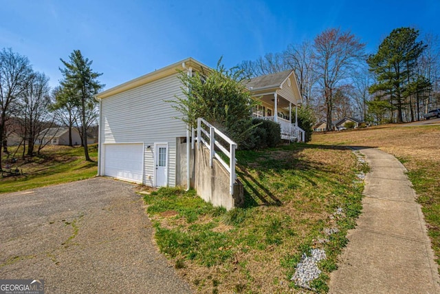 view of side of property featuring aphalt driveway, covered porch, a lawn, and a garage