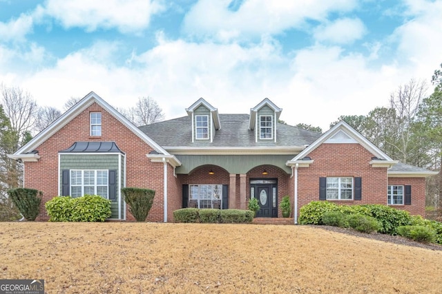 view of front facade with brick siding, a front yard, and a shingled roof