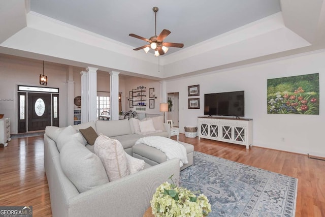 living room featuring a tray ceiling, crown molding, wood finished floors, and ceiling fan