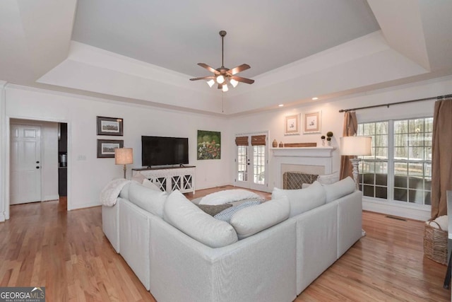 living area with light wood-type flooring, visible vents, a tray ceiling, a fireplace, and ceiling fan