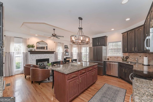 kitchen featuring light wood-type flooring, a sink, tasteful backsplash, stainless steel appliances, and a fireplace