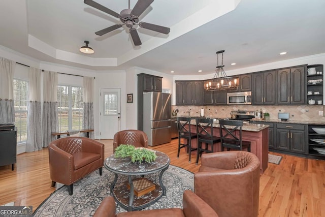 living room with light wood-style flooring, crown molding, ceiling fan with notable chandelier, and a raised ceiling