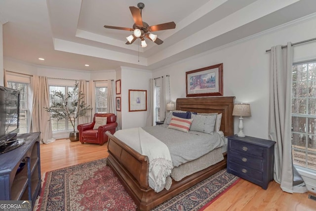 bedroom with multiple windows, light wood-type flooring, a tray ceiling, and ornamental molding