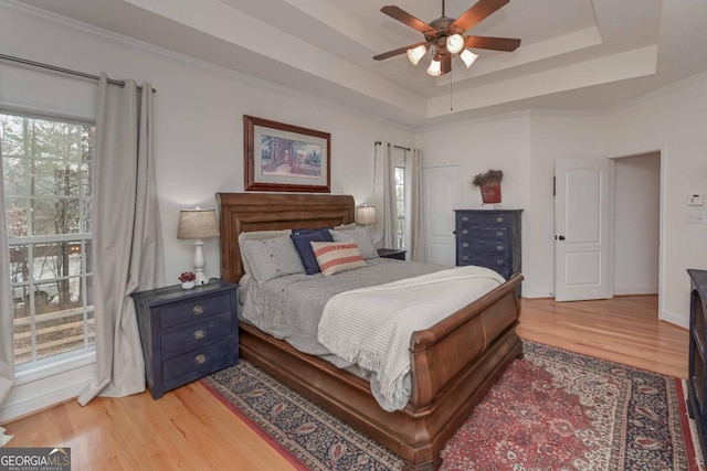 bedroom with light wood finished floors, baseboards, a tray ceiling, and ornamental molding