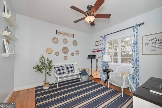 living area featuring baseboards, a ceiling fan, and wood finished floors