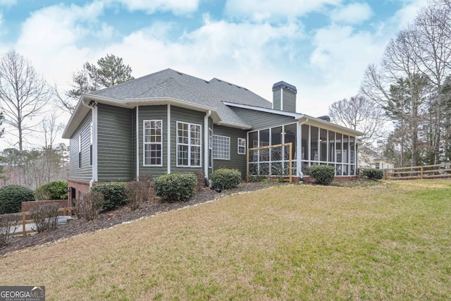 back of property with a lawn, fence, roof with shingles, a sunroom, and a chimney