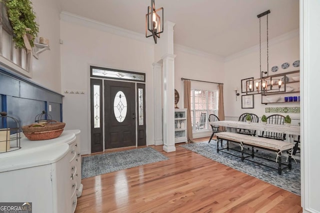 entrance foyer with light wood-style flooring, decorative columns, a chandelier, and ornamental molding