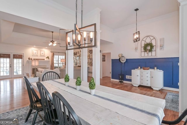 dining area featuring wood finished floors, a wainscoted wall, french doors, crown molding, and ceiling fan with notable chandelier