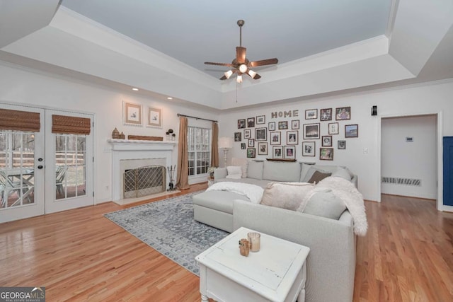 living area featuring a tray ceiling, light wood-style flooring, a ceiling fan, and visible vents