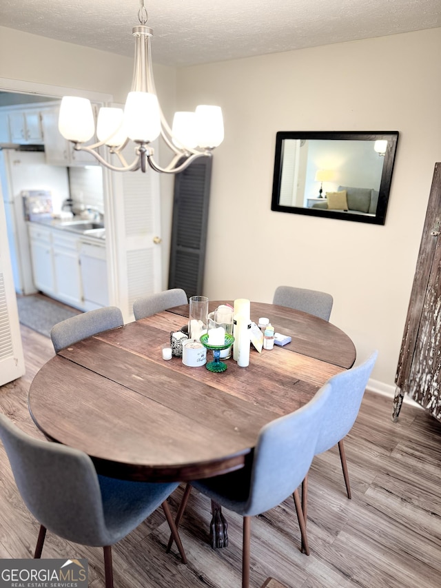 dining room with a notable chandelier, a textured ceiling, light wood-type flooring, and baseboards