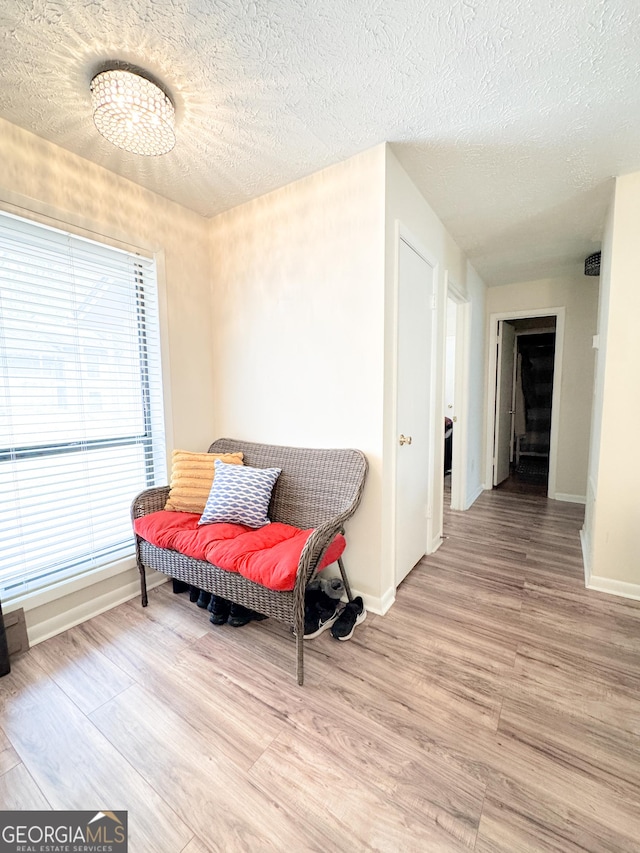 sitting room with a textured ceiling, light wood-type flooring, and baseboards