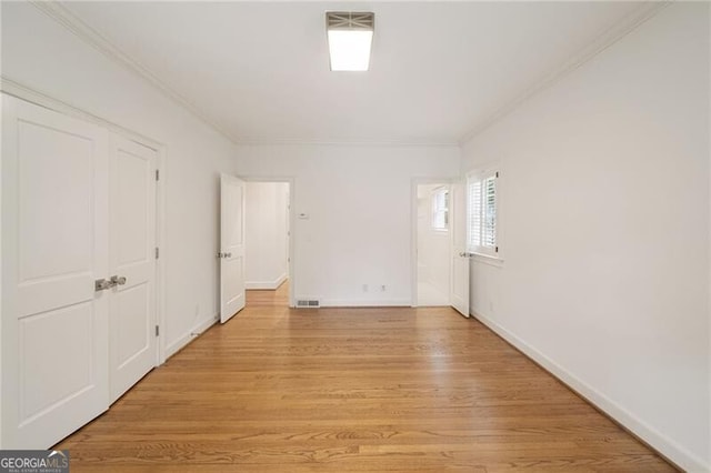 empty room featuring crown molding, light wood-style floors, visible vents, and baseboards