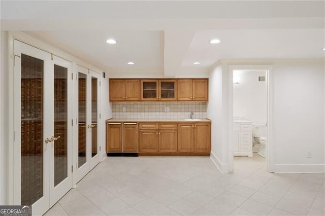 kitchen with brown cabinetry, a sink, light countertops, french doors, and tasteful backsplash